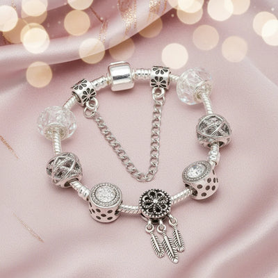 Charm-Armband Traumfeder in Silber mit Traumfänger-Anhänger, klaren Glasperlen und Sicherheitskette auf rosa Seide