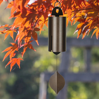 Windspiel aus Metall mit einem Klangrohr in Bronzebraun, hängend vor orangem Herbstlaub im Garten