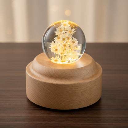 Cremegelbe Margeriten in einer 6 cm Kugel aus klarem Kunstharz auf hohem, rundem Holzsockel, warm leuchtend