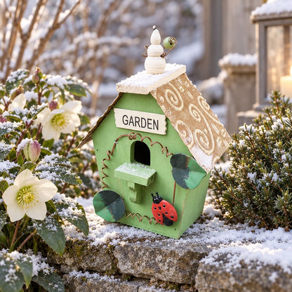 Grünes Holz Vogelhaus mit Garden Schild und Marienkäfer auf verschneiter Steinmauer neben Christrosen im Winter